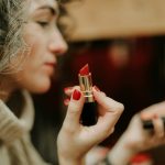 woman in gray sweater holding lipstick