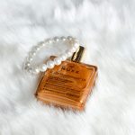 From above golden face oil in refined bottle placed with pearl bracelet on white cozy plaid