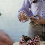Crop anonymous African American female opening mirror at table with cosmetic bag on blurred background