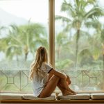 woman sitting on white cushion near glass window